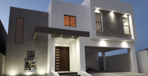 Fachada de casa moderna en tonos blanco y gris, iluminada con luces LED al anochecer, destacando el contraste térmico generado por los colores en la superficie.