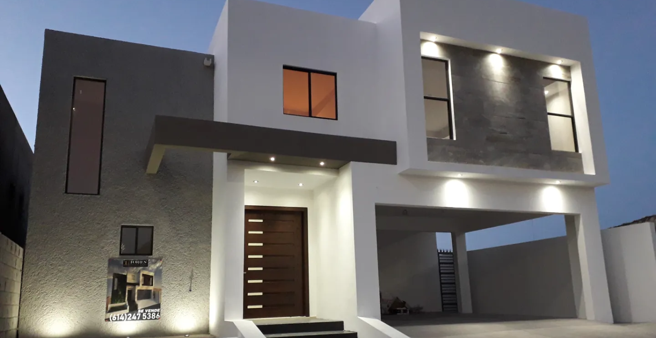 Fachada de casa moderna en tonos blanco y gris, iluminada con luces LED al anochecer, destacando el contraste térmico generado por los colores en la superficie.